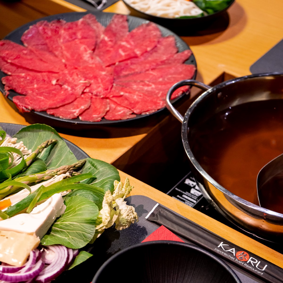 Gedeckter Shabu-Shabu-Tisch bei KAORU Mannheim mit Rindfleischplatte, Gemüseplatte und Topf